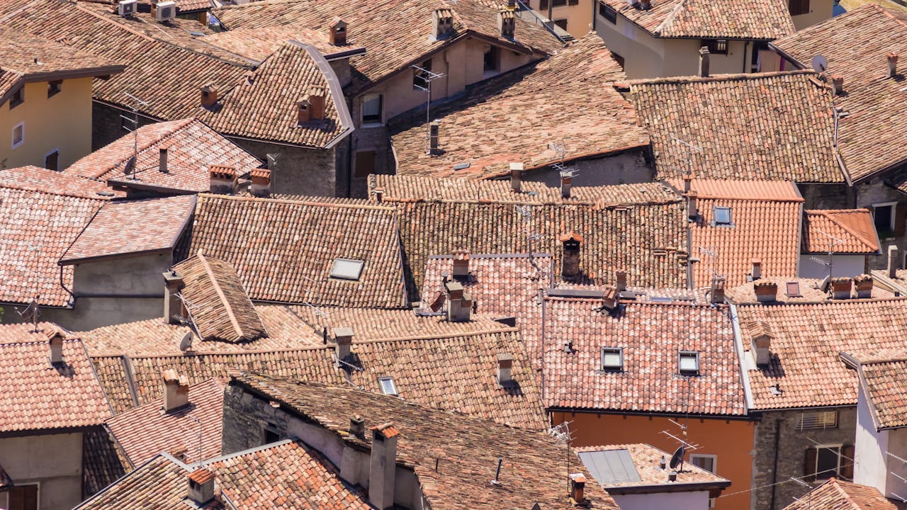 Close-up aerial shot of traditional European terracotta rooftops under bright sunlight.